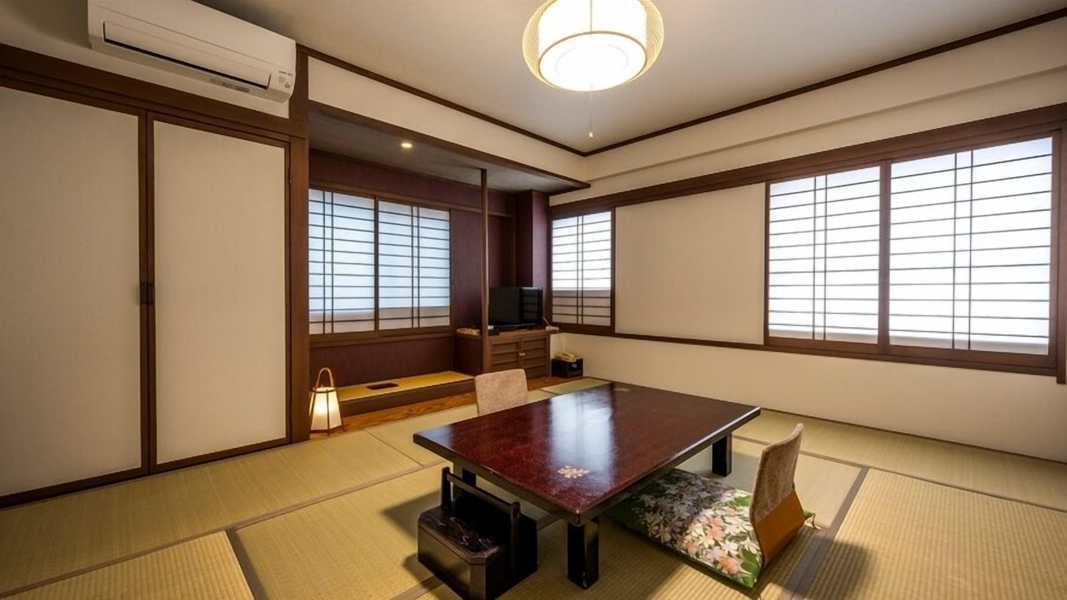 Una habitación japonesa tradicional con suelo de tatami, una mesa baja, puertas correderas y un televisor.