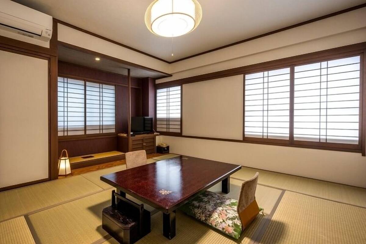 Una habitación japonesa tradicional con suelo de tatami, una mesa baja, puertas correderas y un televisor.