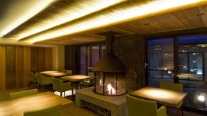 Un restaurante acogedor con mesas y sillas de madera, una chimenea de piedra y vistas de la ciudad por la noche.