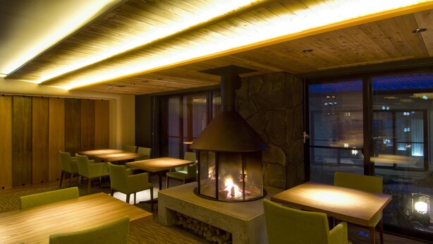 Un restaurante acogedor con mesas y sillas de madera, una chimenea de piedra y vistas de la ciudad por la noche.