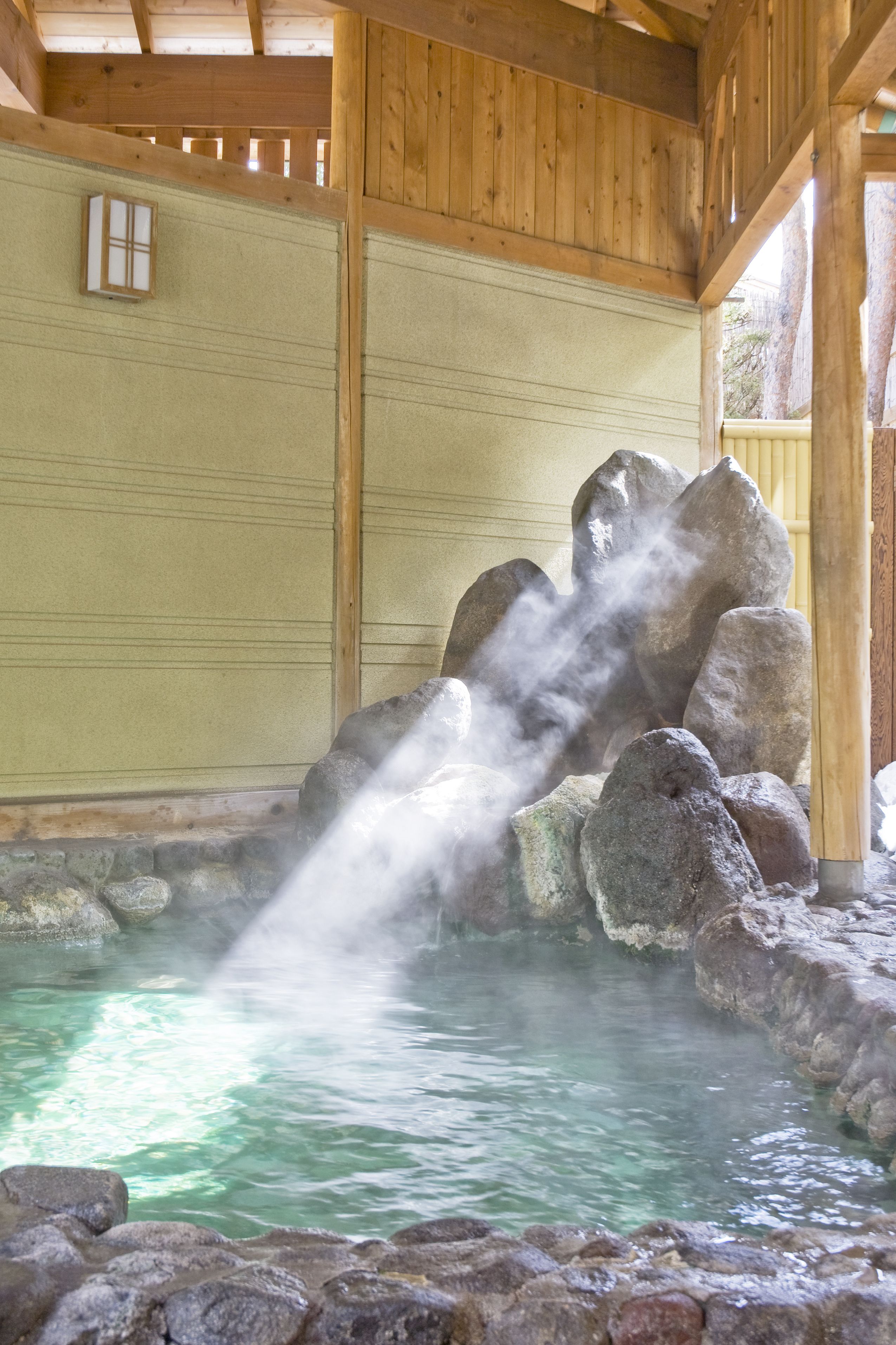 A hot spring area with a wooden structure, a stone basin, and steam rising from the water.