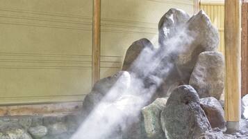 A hot spring area with a wooden structure, a stone basin, and steam rising from the water.