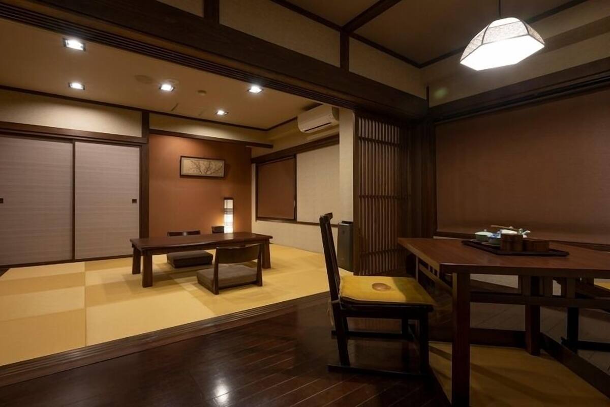 Una habitación tradicional japonesa con suelo de tatami, una mesa baja, una silla y puertas correderas.