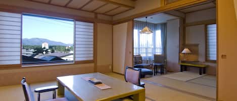 A traditional Japanese room with tatami flooring, a low table with cushions, and a view of mountains through large windows.