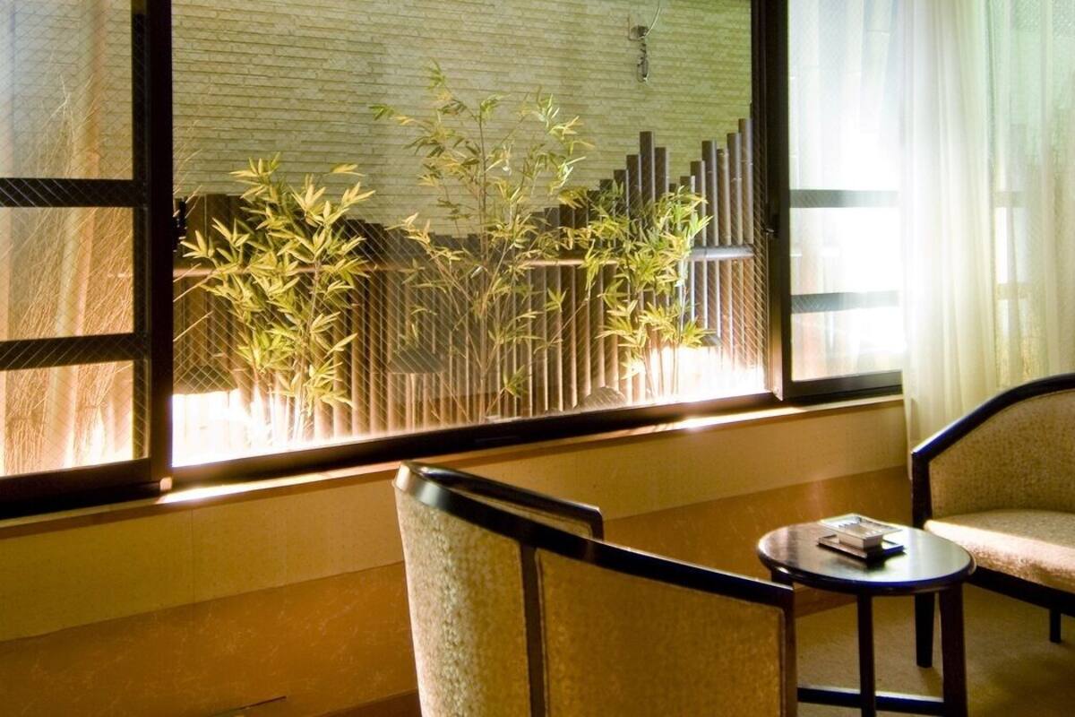 Una habitación con vistas a plantas de bambú a través de una ventana, una silla, una mesita y una cama.