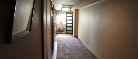 A hallway with patterned carpet, a door at the end, and a light fixture on the ceiling.