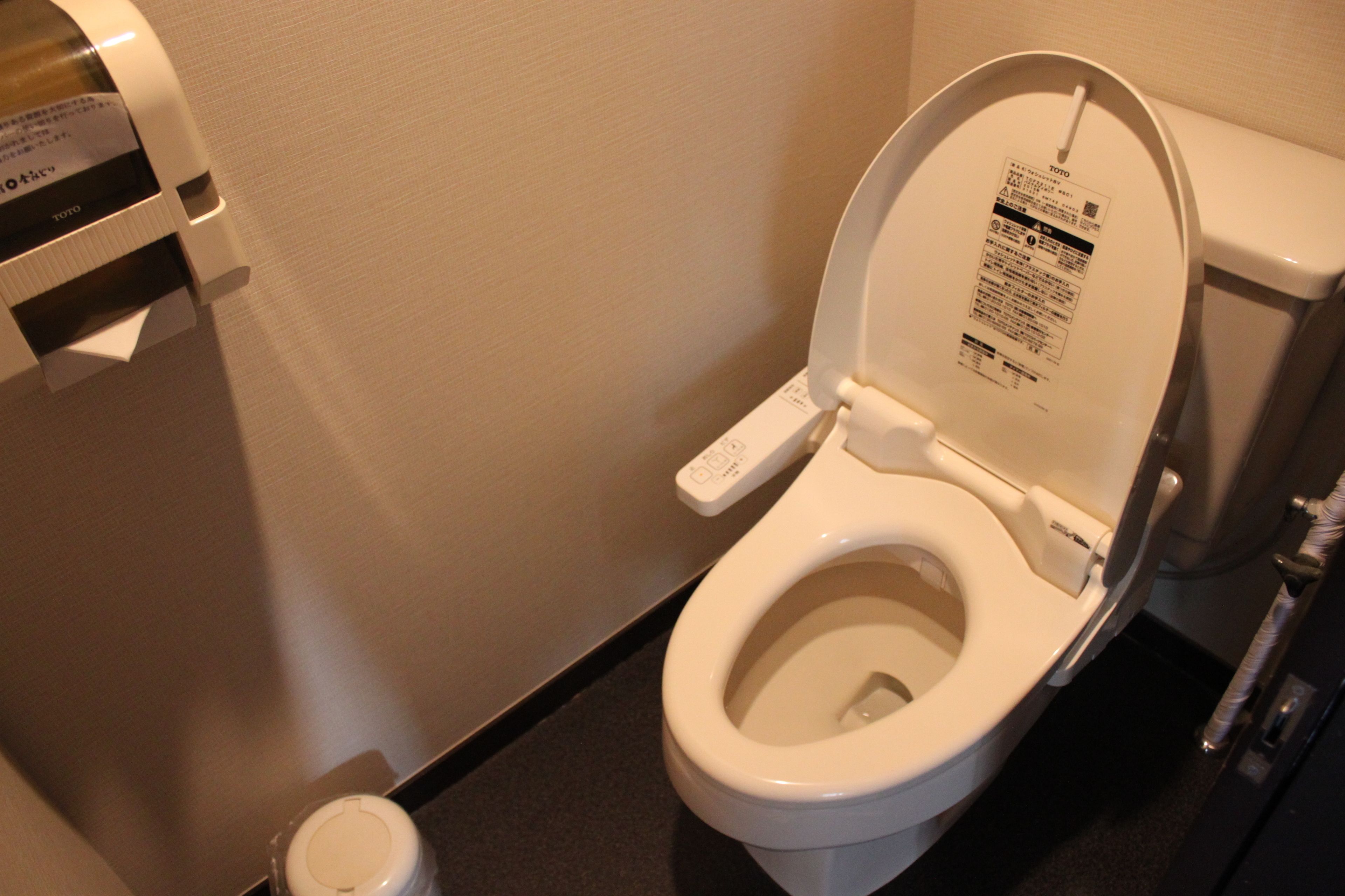 Inodoro con una etiqueta en la tapa y dispensador de papel a la izquierda.