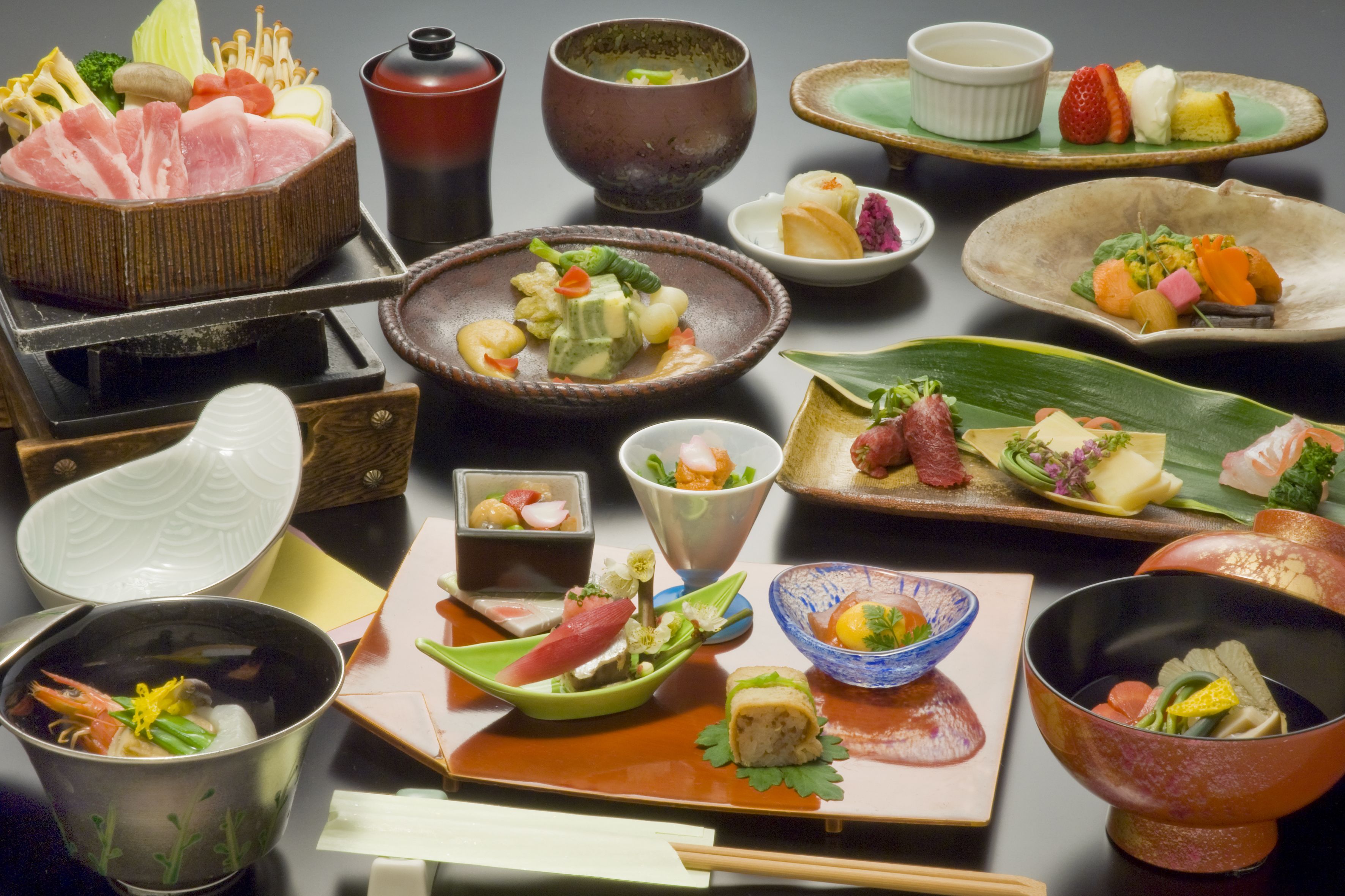 A variety of Japanese dishes including sushi, sashimi, and tempura, served on traditional ceramic and metalware.