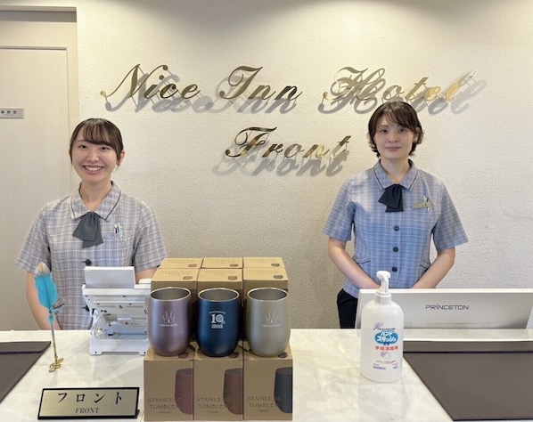 Two staff members at a hotel reception desk with a sign reading 'Nice Inn Hotel Front'. - Nice Inn Hotel Ichikawa Tokyo Bay (Ichikawa)