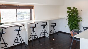 A modern kitchen with dark wood flooring, a white countertop, and three black bar stools. - Nice Inn Hotel Ichikawa Tokyo Bay (Ichikawa)