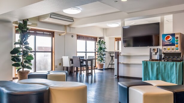 A modern hotel lobby with seating areas, a dining table, and a large flat-screen TV. - Nice Inn Hotel Ichikawa Tokyo Bay (Ichikawa)