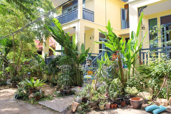 A courtyard with various potted plants, a small garden area, and a building with balconies. - Baan Patcharintorn Samui (Koh Samui)