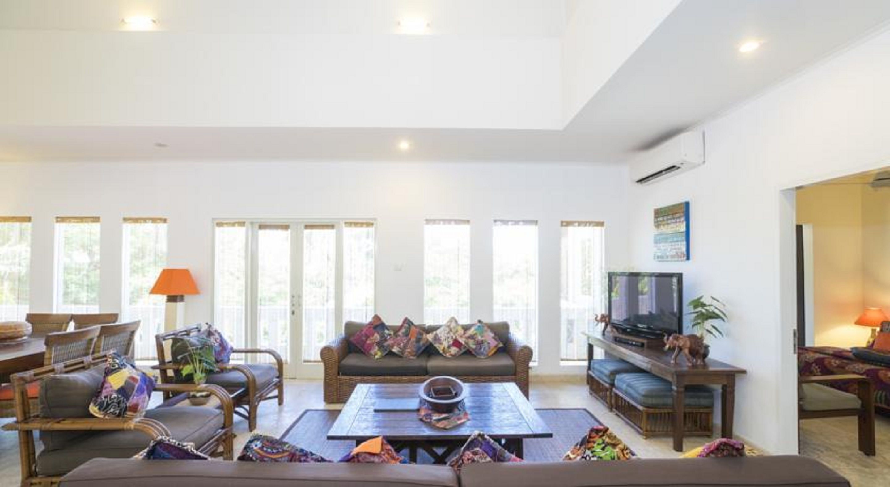 A spacious living room with a sofa, coffee table, and television. Large windows provide natural light.
