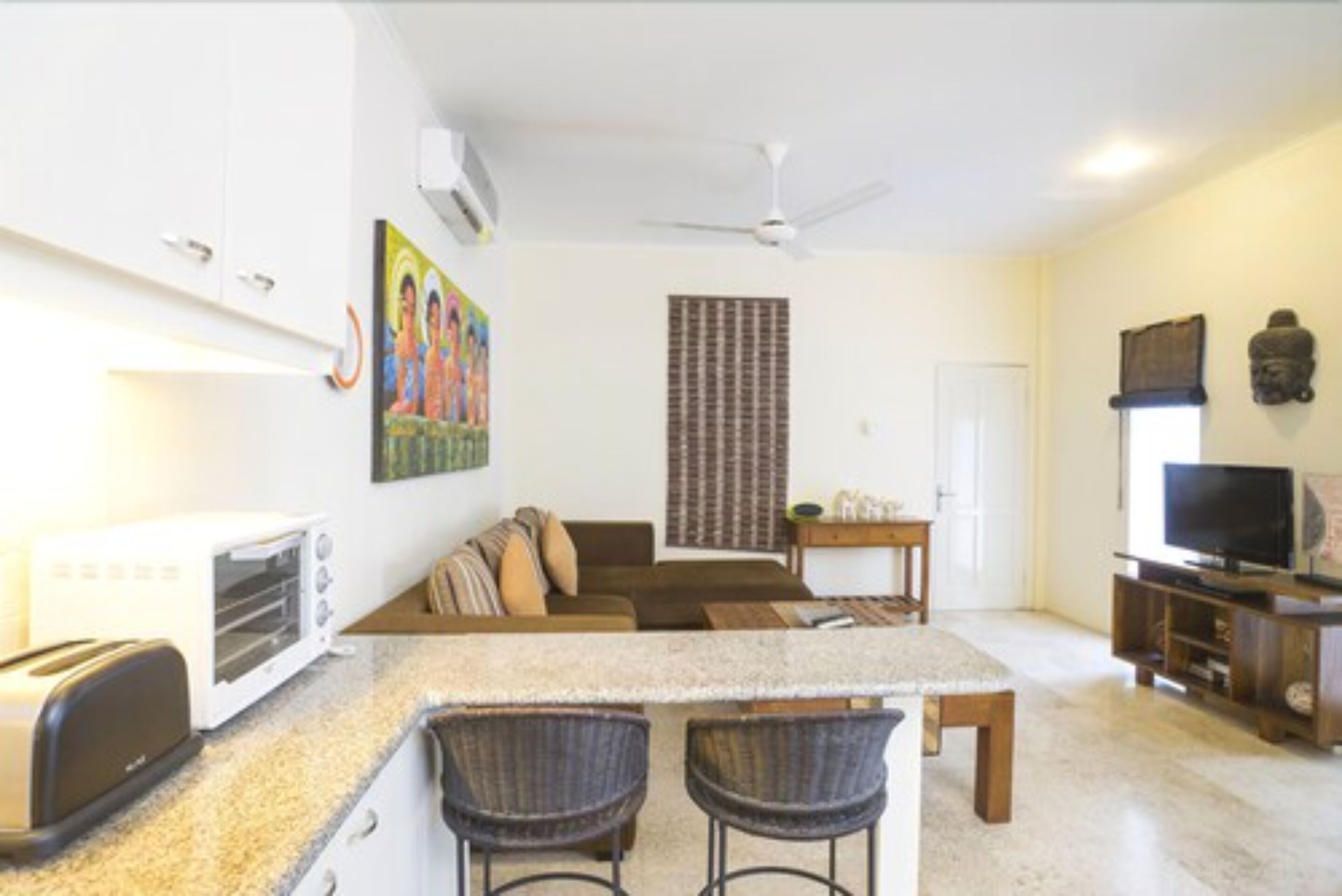 Een moderne keuken met een ingebouwde toaster, een eethoek met een tafel en stoelen, een woonkamer met een bank en een televisie, en een plafondventilator.