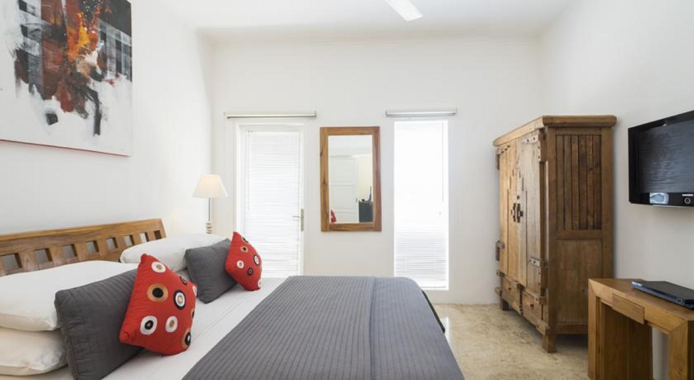 A bedroom with a bed, pillows, a wooden wardrobe, a television, and a mirror.