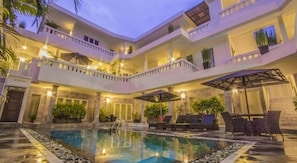 Ein Hotel mit mehreren Etagen, einem zentral gelegenen Pool, Außenbereich zum Sitzen und Balkonen.