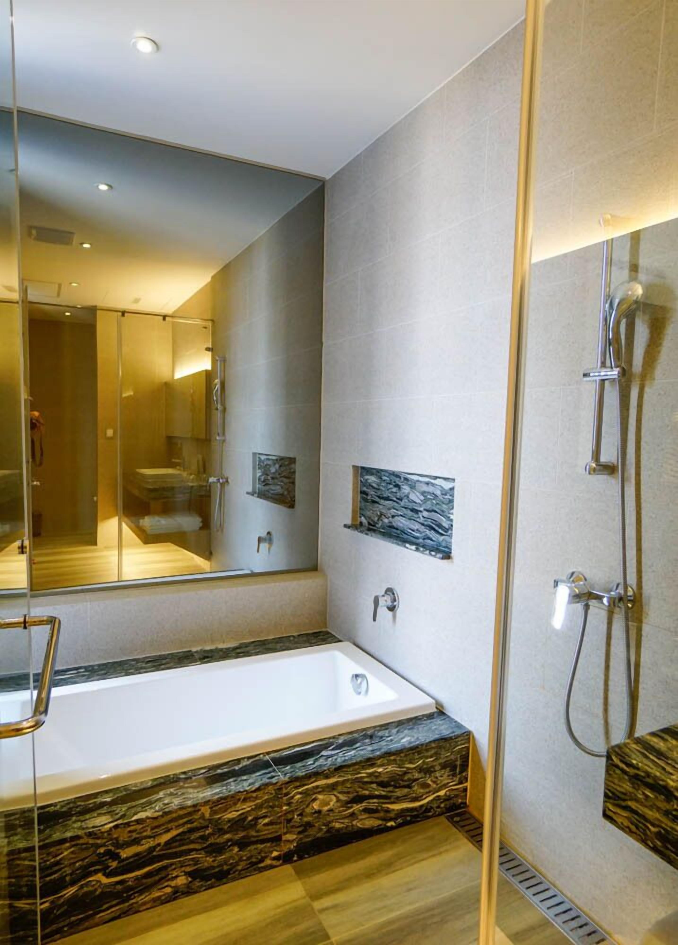 A modern bathroom with a glass-enclosed shower, a marble-topped bathtub, and a large mirror.
