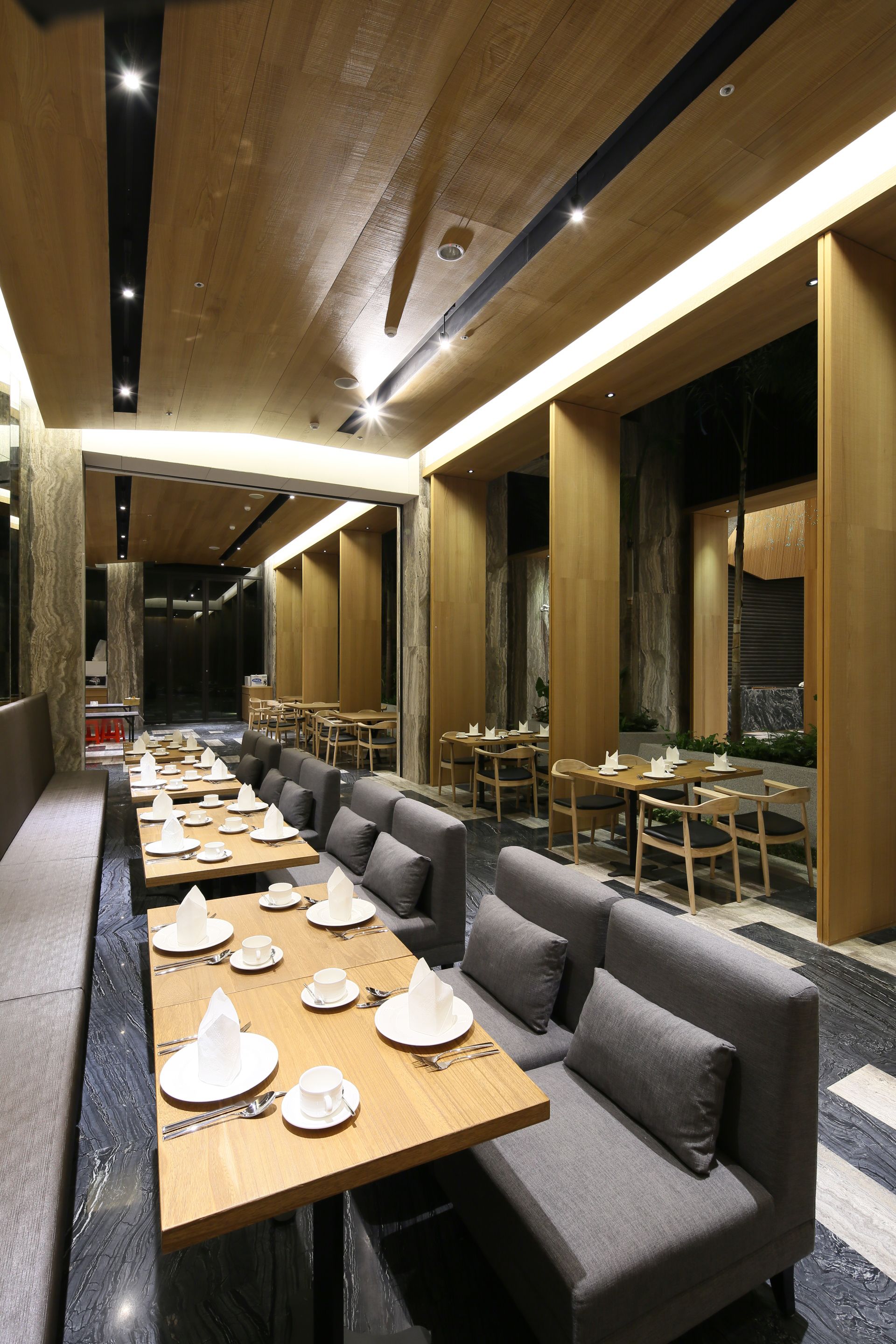 A modern restaurant with long communal tables and cushioned seating areas.