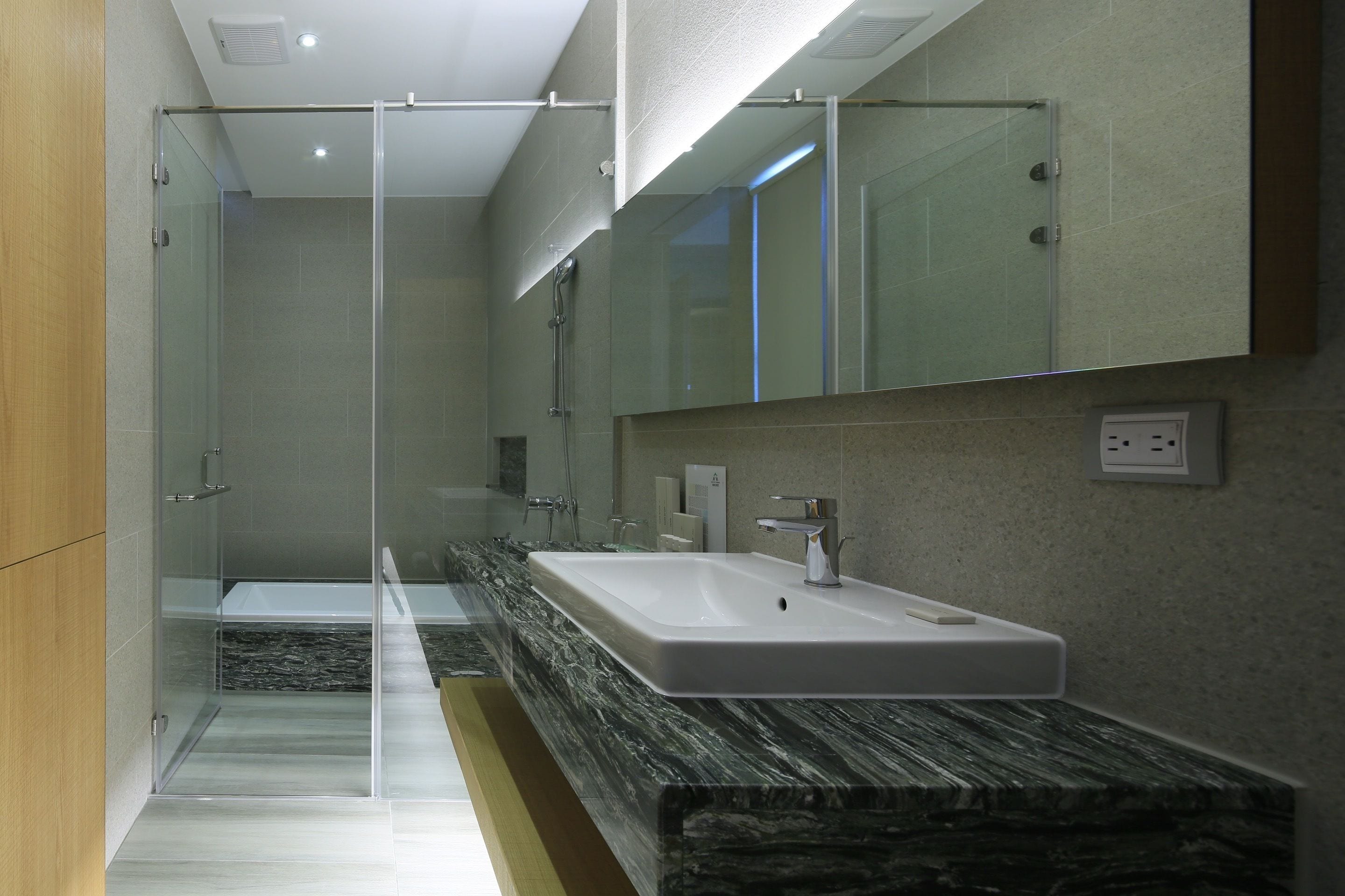 A modern bathroom with a glass shower enclosure, a marble countertop, and a large mirror above the sink.