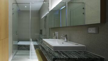 A modern bathroom with a glass shower enclosure, a marble countertop, and a large mirror above the sink.