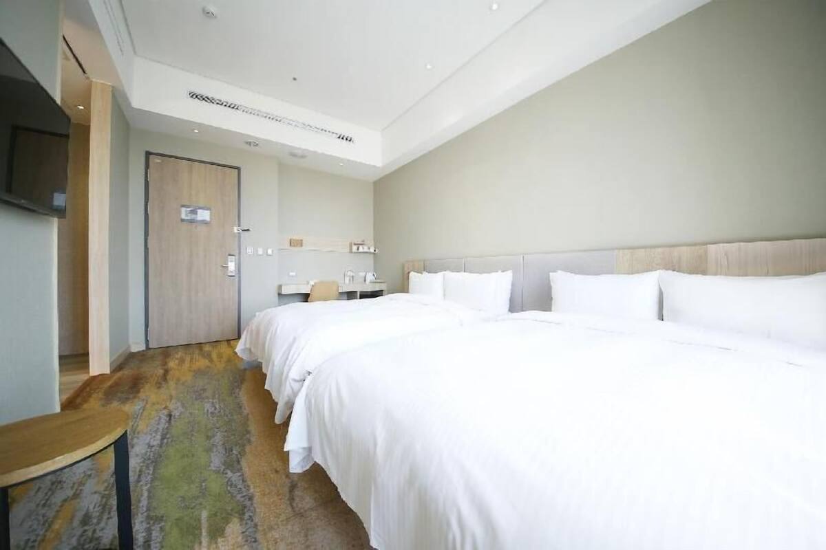 Habitación de hotel con dos camas, un escritorio, una silla, un televisor y una puerta.