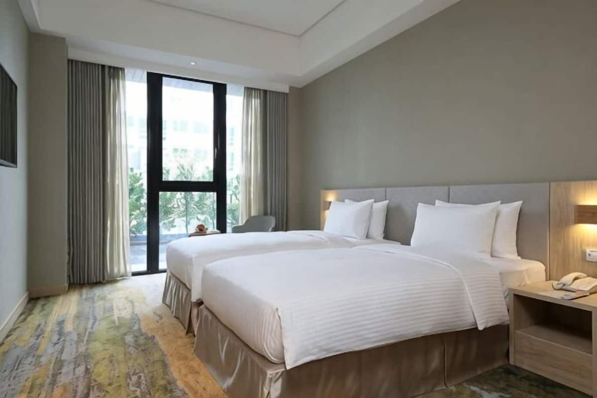 Una habitación de hotel con dos camas, un escritorio, una silla y un ventanal grande.