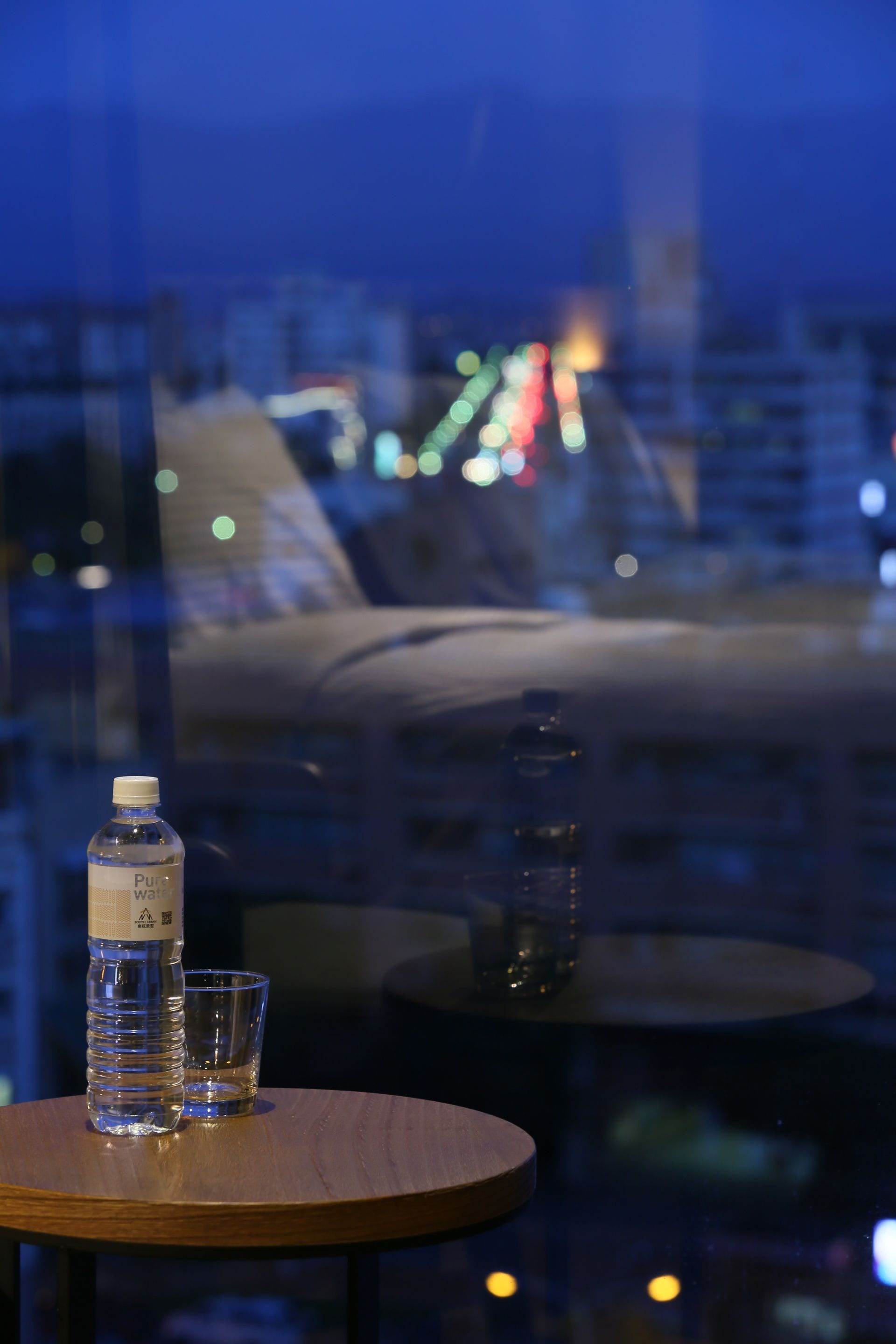 A table with a water bottle and a glass, a sofa, and a view of a cityscape at night.
