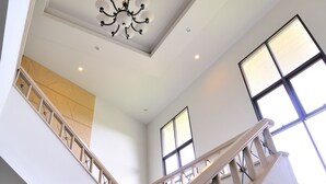 Un interior moderno con una escalera, una araña y ventanas amplias.