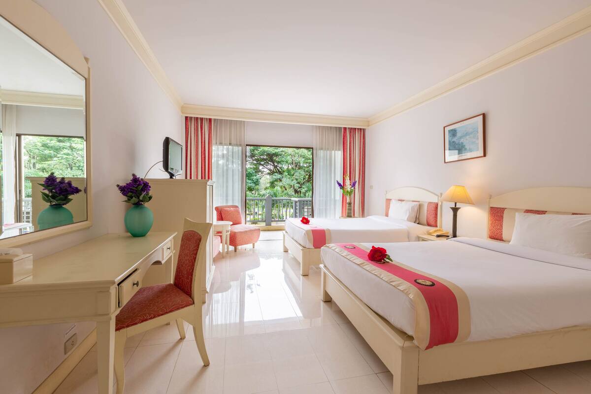 Una habitación de hotel con cama, escritorio, silla, televisión y ventana con cortinas.