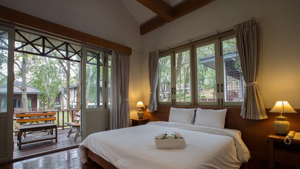 Un dormitorio con una cama grande, cabecera de madera y dos lámparas de noche. Se ve una ventana con cortinas y vistas al exterior.
