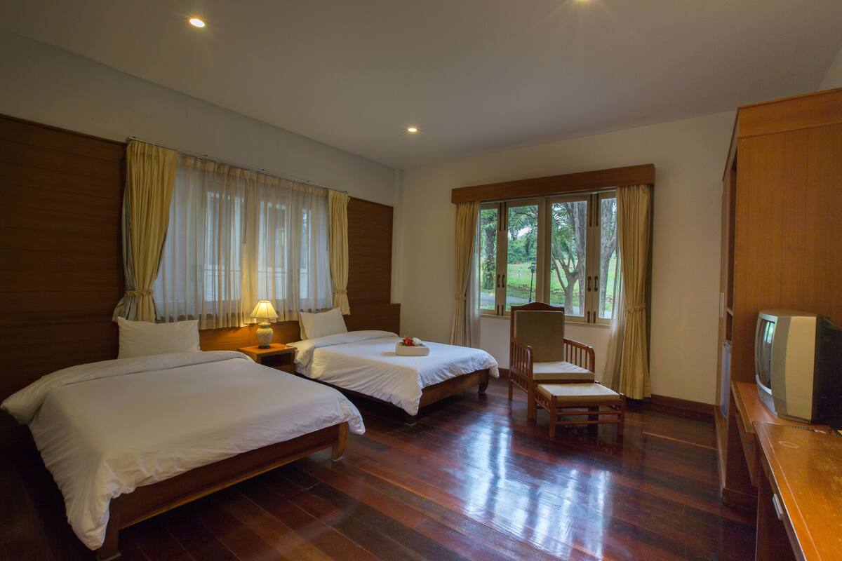Habitación de hotel con dos camas, piso de madera, televisión y ventana con cortinas.