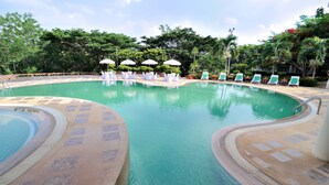 Una piscina con sillones de descanso y sombrillas, rodeada de vegetación.