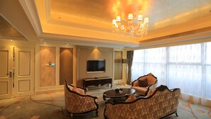 A spacious living room with a chandelier, a flat-screen TV, and a sofa set.