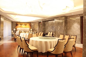 A conference room with a round table, multiple chairs, a chandelier, marble walls, and a large painting on the back wall.