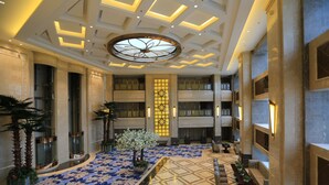 A spacious lobby with a high ceiling, a central decorative light fixture, and a patterned floor.