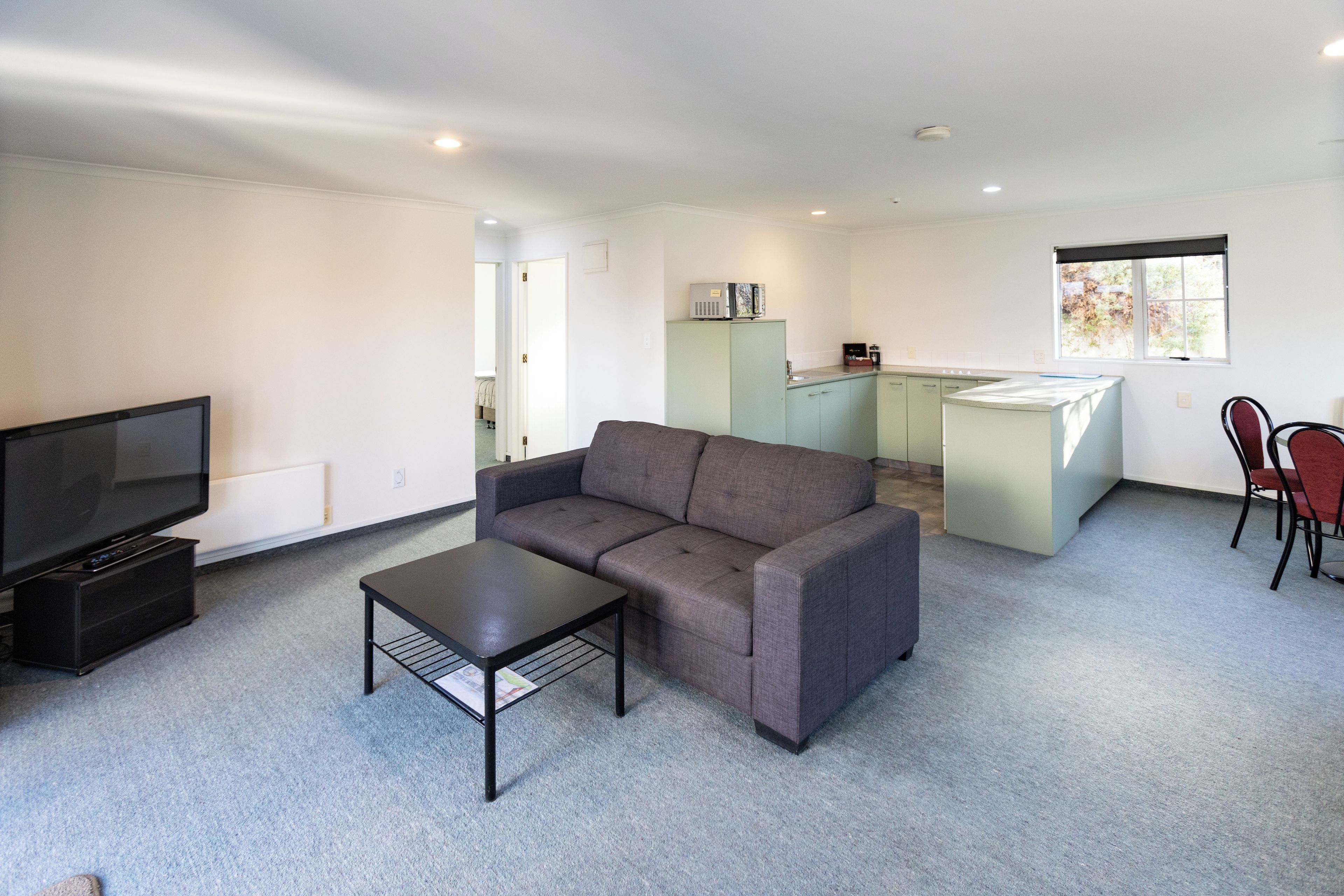 A modern living room with a sofa, a coffee table, a TV, and a kitchenette area.