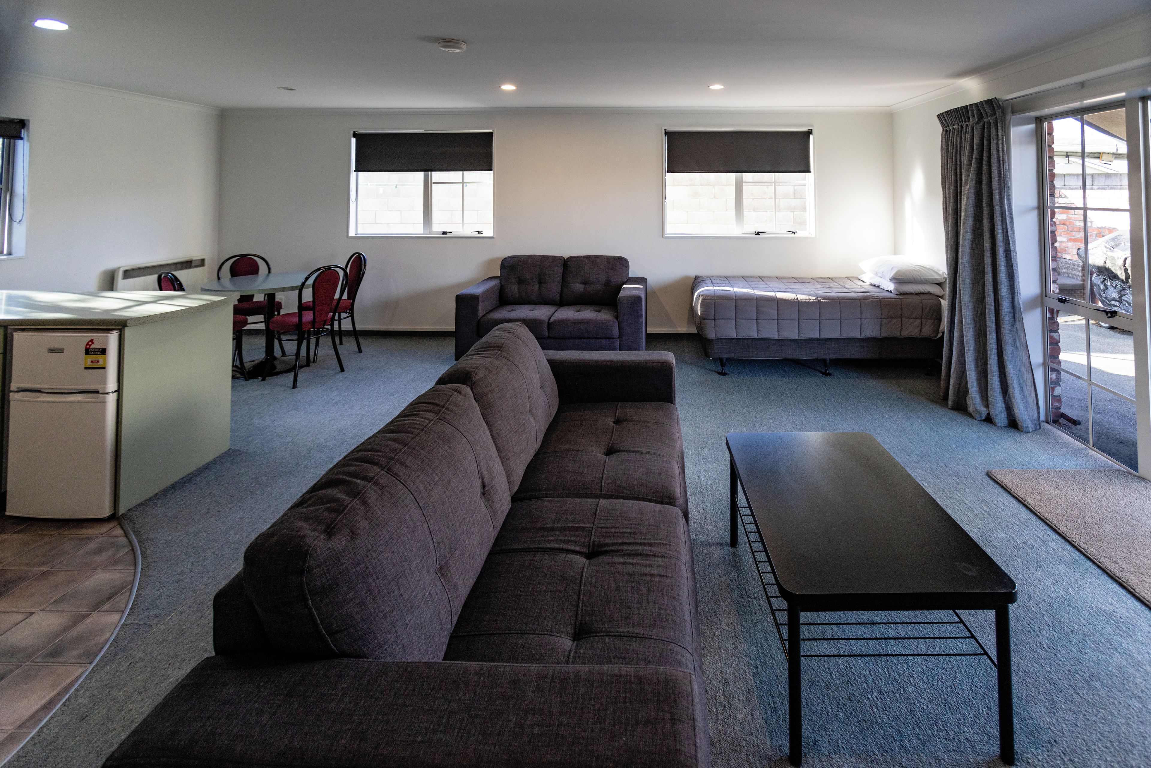Een kamer met een bank, een eettafel met stoelen, een bed en een kleine kitchenette.