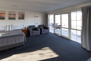 A hotel room with a bed, two armchairs, a small table, a floor lamp, and a large window with curtains. - Alexandra Heights Motel (Alexandra)