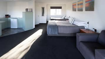 Habitación de hotel moderna con kitchenette, cama con cubrecama gris, sofá gris y un amplio ventanal que proporciona luz natural.