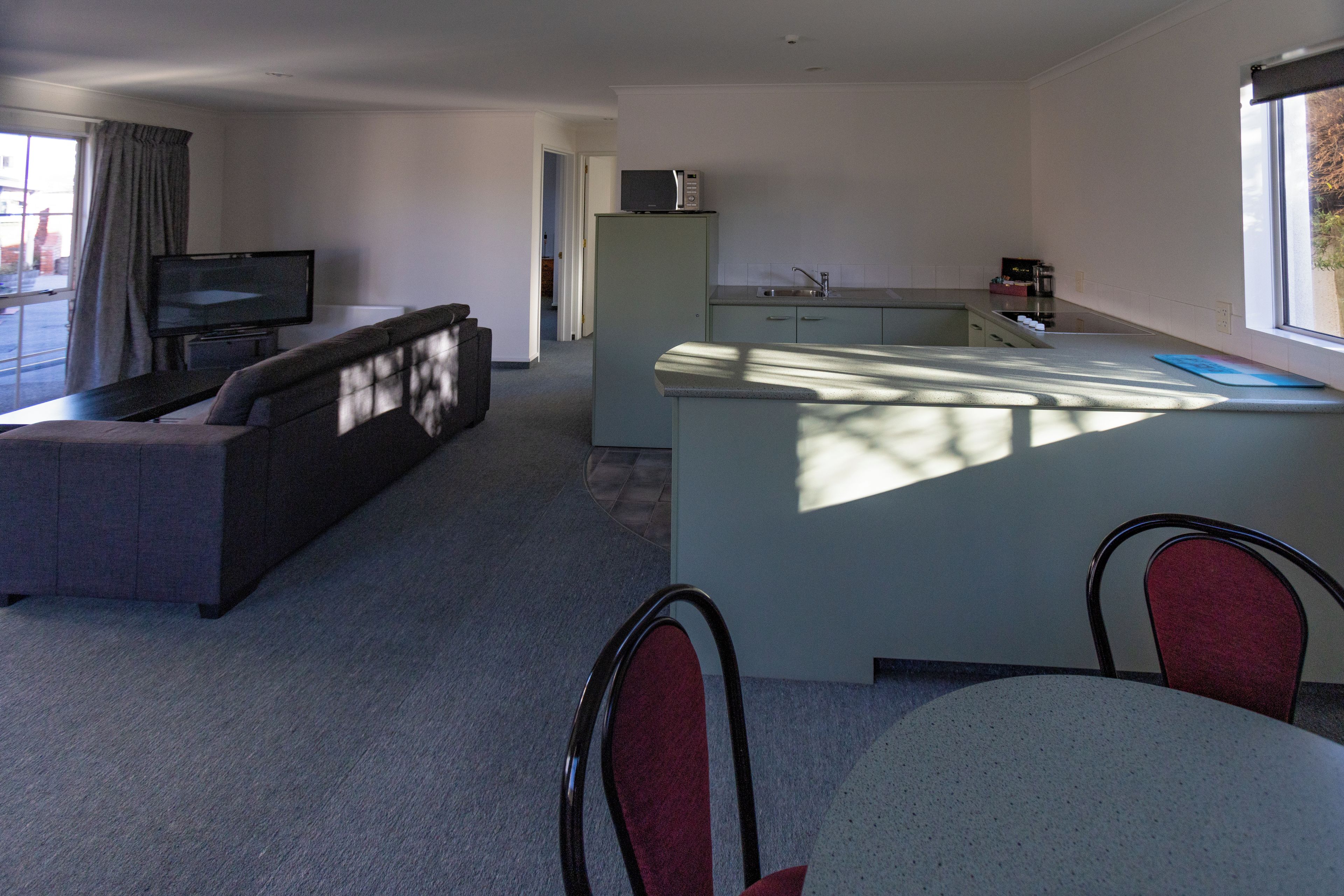 A modern living room with a sofa and a television, a kitchen with a sink and a microwave, and a dining area with chairs.