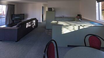 A modern living room with a sofa and a television, a kitchen with a sink and a microwave, and a dining area with chairs.