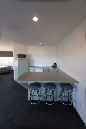 A kitchen with a central island, three bar stools, a microwave, and a refrigerator. - Alexandra Heights Motel (Alexandra)