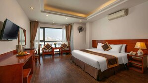 A hotel room with a large bed, a desk with a flat-screen TV, a chair, a small table with a vase, and a window with curtains. - Bounty Hotel (Hanoi)