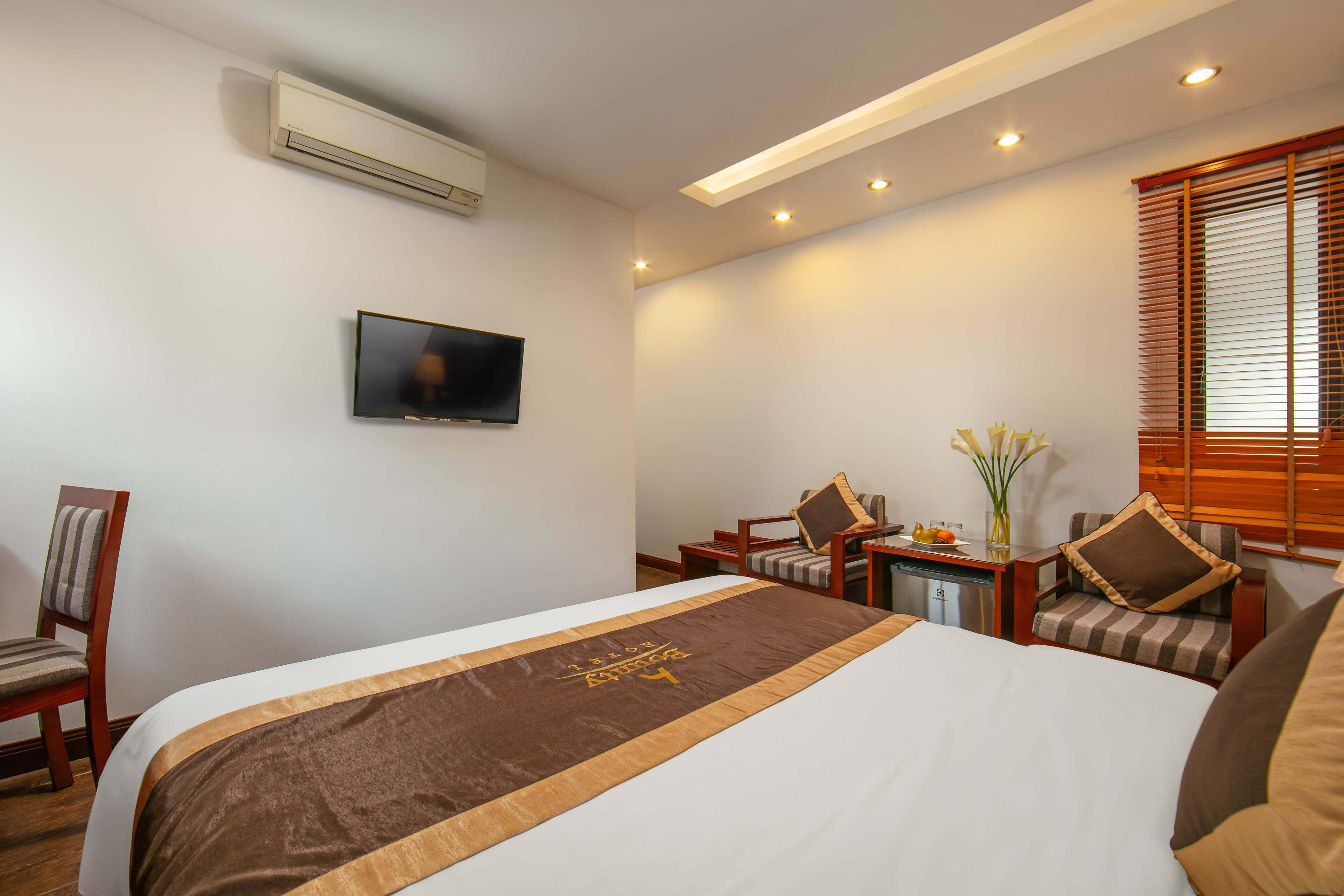 A hotel room with a bed, a television, a desk with a chair, and a window with blinds.