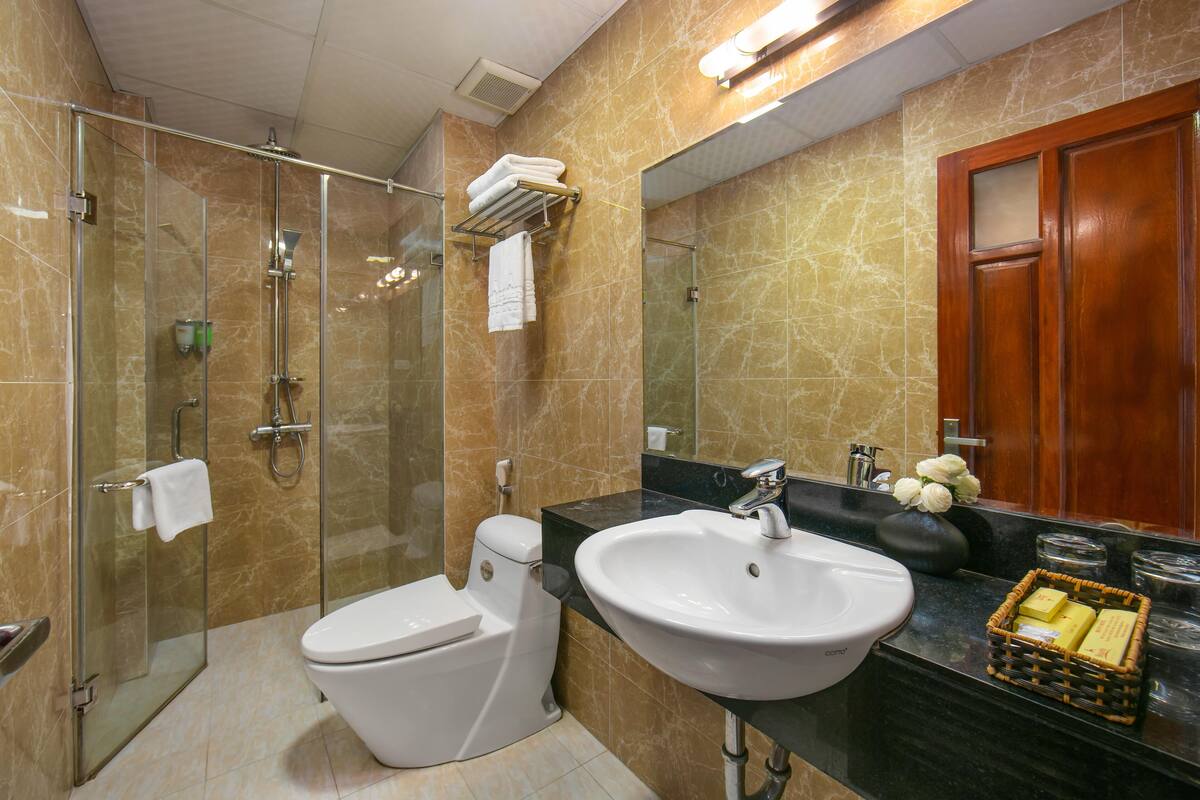 A modern bathroom with a glass-enclosed shower, a white toilet, a large sink, and a wooden door.