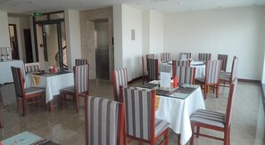 Un coin repas avec des chaises et des tables à rayures, un espace cuisine équipé d’une cuisinière, et une porte avec un panneau de signalisation verte indiquant la sortie.