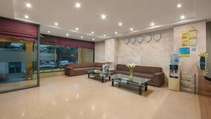 A modern lobby with a glass partition, two sofas, a coffee table, a water dispenser, and clocks on the wall. - Bounty Hotel (Hanoi)