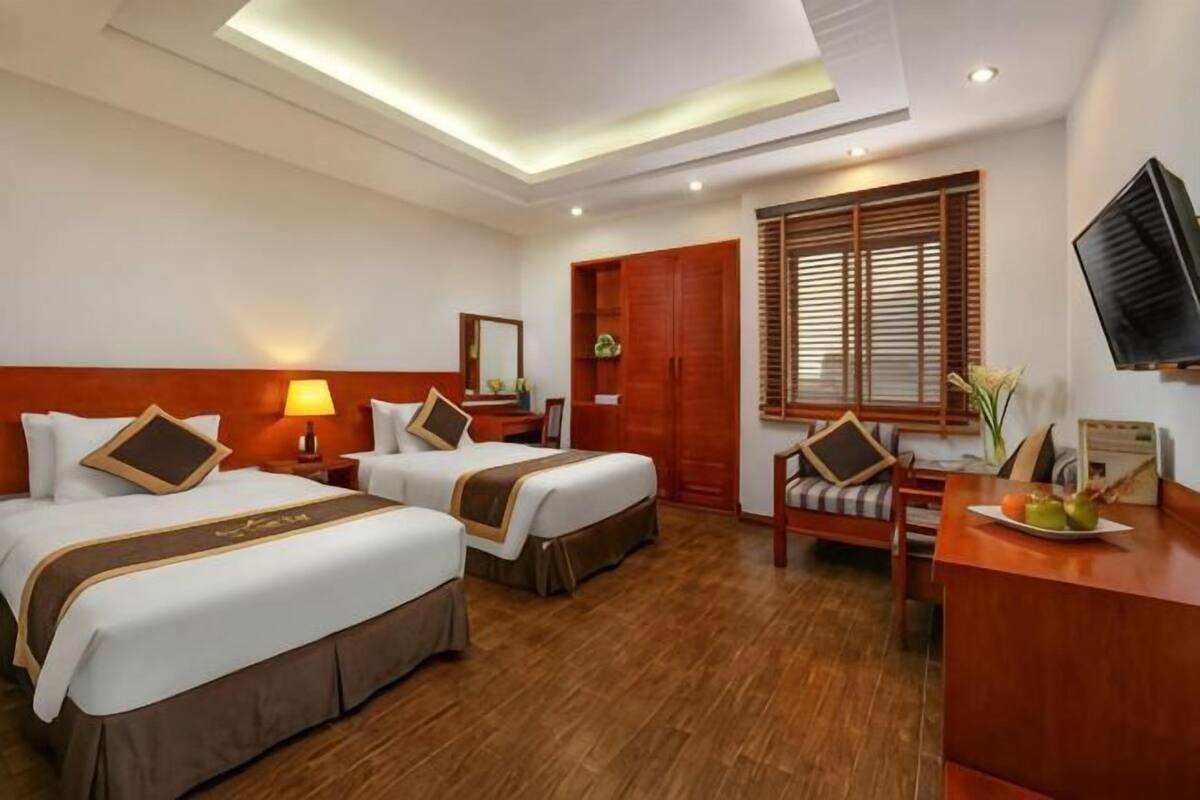 A hotel room with two beds, a desk, a TV, and a window with wooden blinds.