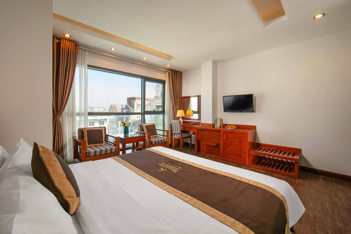 A hotel room with a large bed, a desk, a chair, a television, and a view of the city.