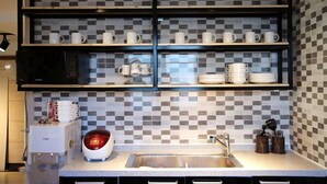 Una cocina con salpicadero a cuadros, tazas blancas en estantes, un microondas y un lavamanos.